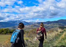 Two women hiking on a mountain trail with scenic views under a blue sky.